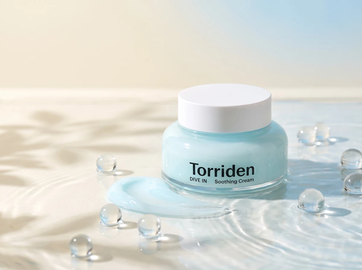 TORRIDEN DIVE IN Soothing Cream jar standing in shallow rippling water with clear water spheres and a swatch of light blue gel-cream, in warm daylight