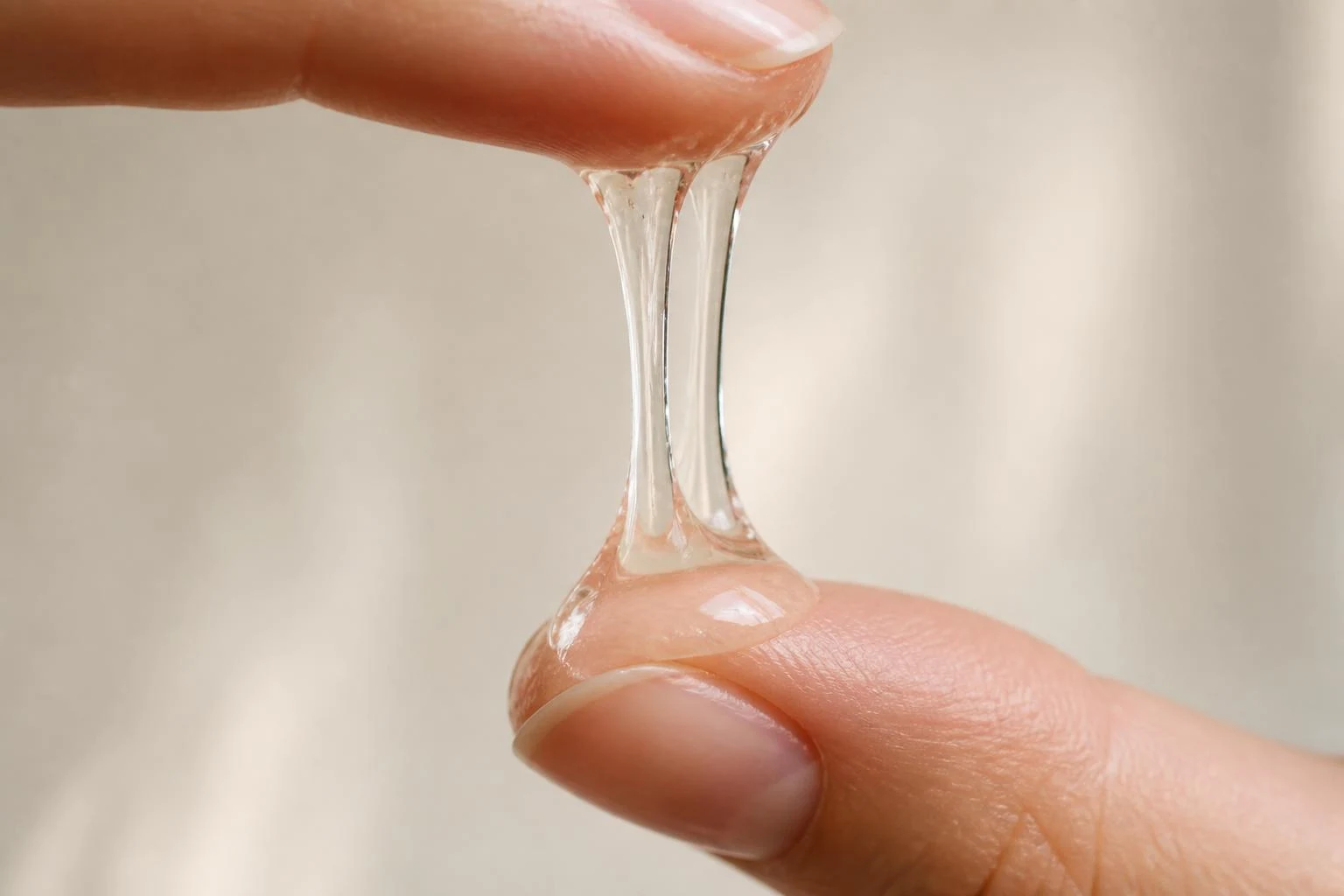 Thick clear mucin gel stretching between two fingertips